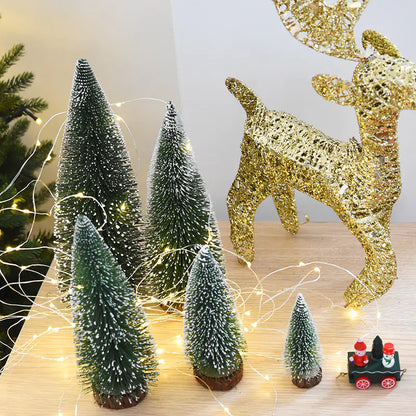 Decorative setup with miniature Christmas trees, a gold glittery reindeer, and string lights on a wooden surface.
