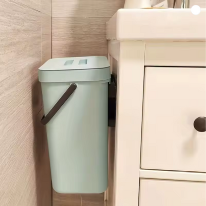 Light green trash can with a brown handle attached to a beige cabinet in a bathroom setting.