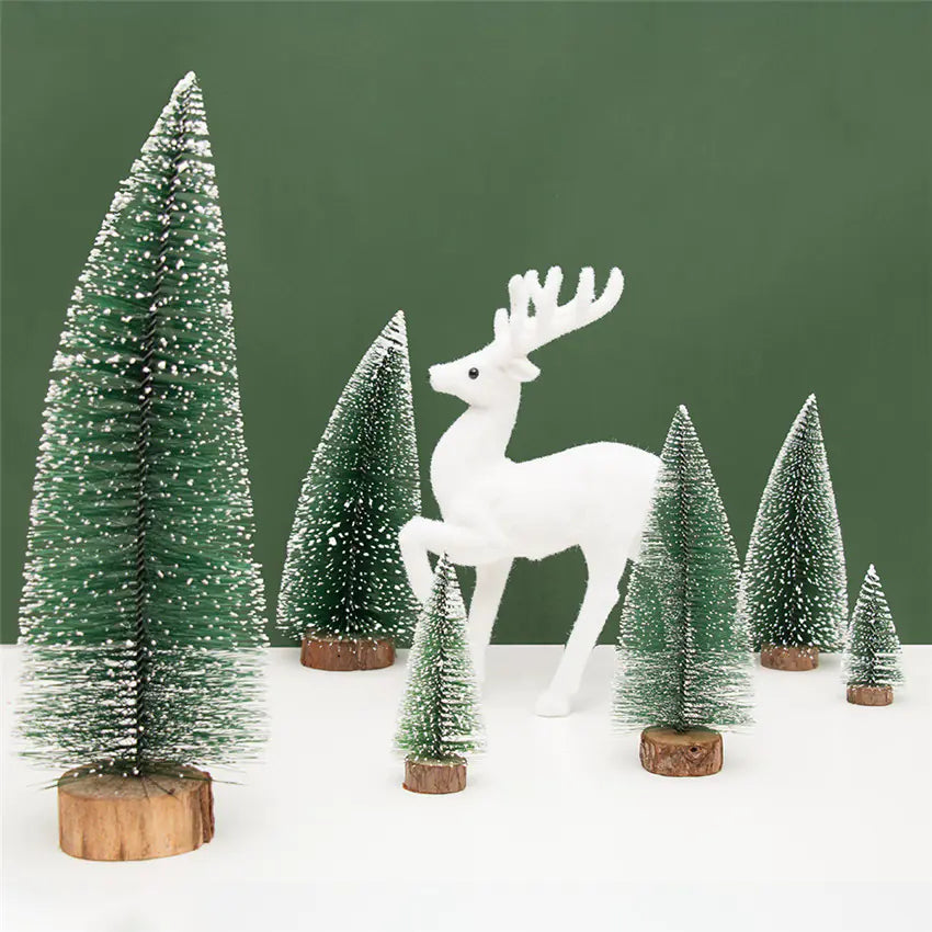 White deer figure standing among miniature snow-covered trees on a white surface with a green background